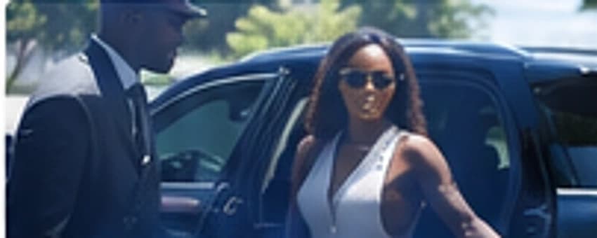 A chauffeur holding the door of a dark SUV for a woman stepping out